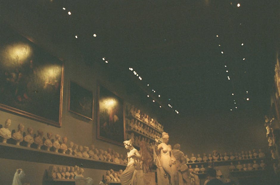 Dimly lit museum gallery showcasing sculptures, busts, and classical paintings.